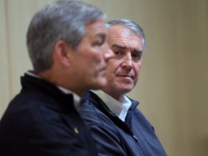 Barta looks on with Kirk Ferentz in the foreground, speaking at a press conference